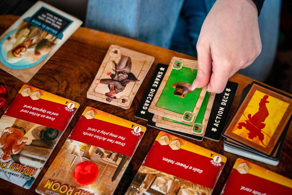 Players place a green card on the table during a game of Indiana Jones: Sands of Adventure.