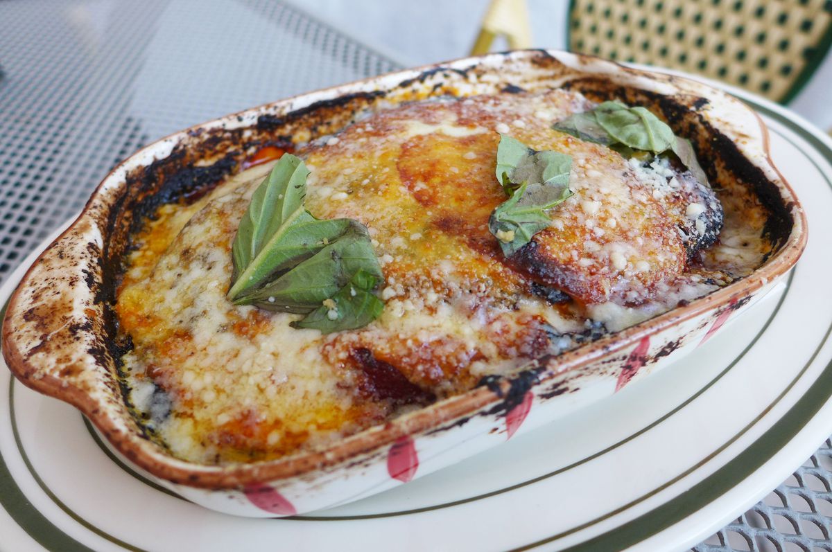 A rectangular casserole with cheese and basil leaves on top, blackened around the edges.