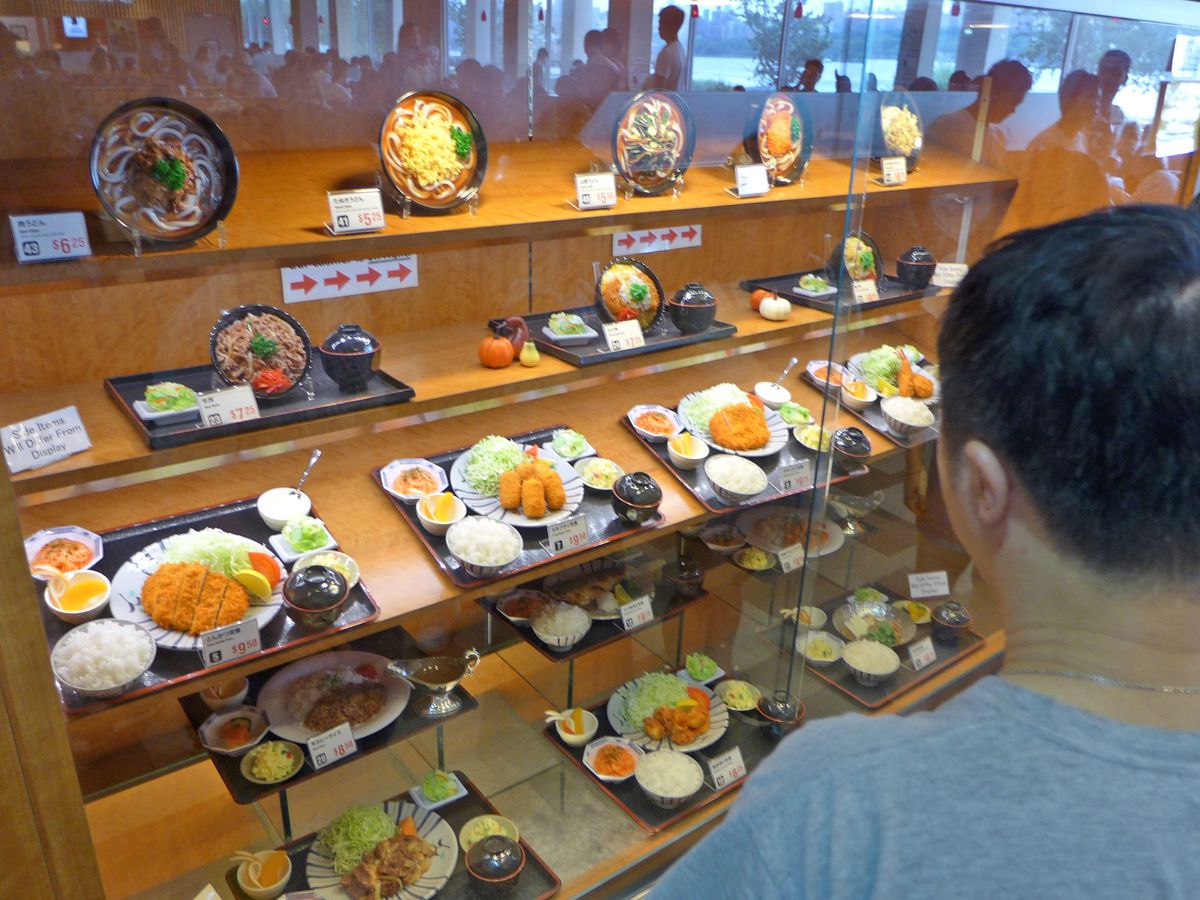 A glass case filled with mock ups of over a dozen full plate dishes as a guy looks on.