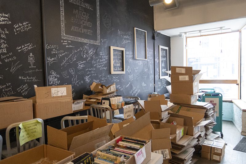 Storage boxes and free book giveaways are piled up near a wall in Volume Bookcafe on Friday, March 26, 2021. The wall is filled with signatures from artists, authors and other celebrity visitors. The store’s last day is Saturday.