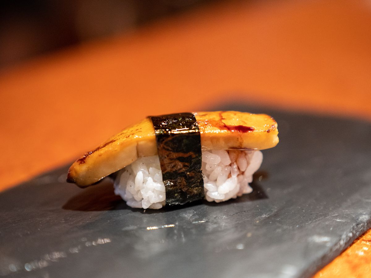 A single piece of foie gras nigiri on a black platter.