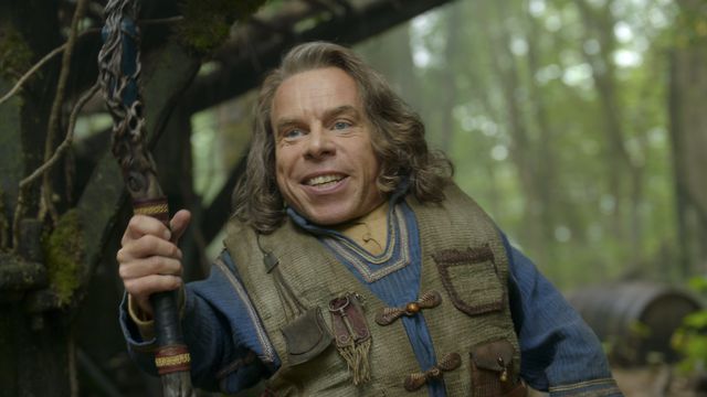 Warwick Davis grins, holding a staff, as Willow Ufgood in Willow. 