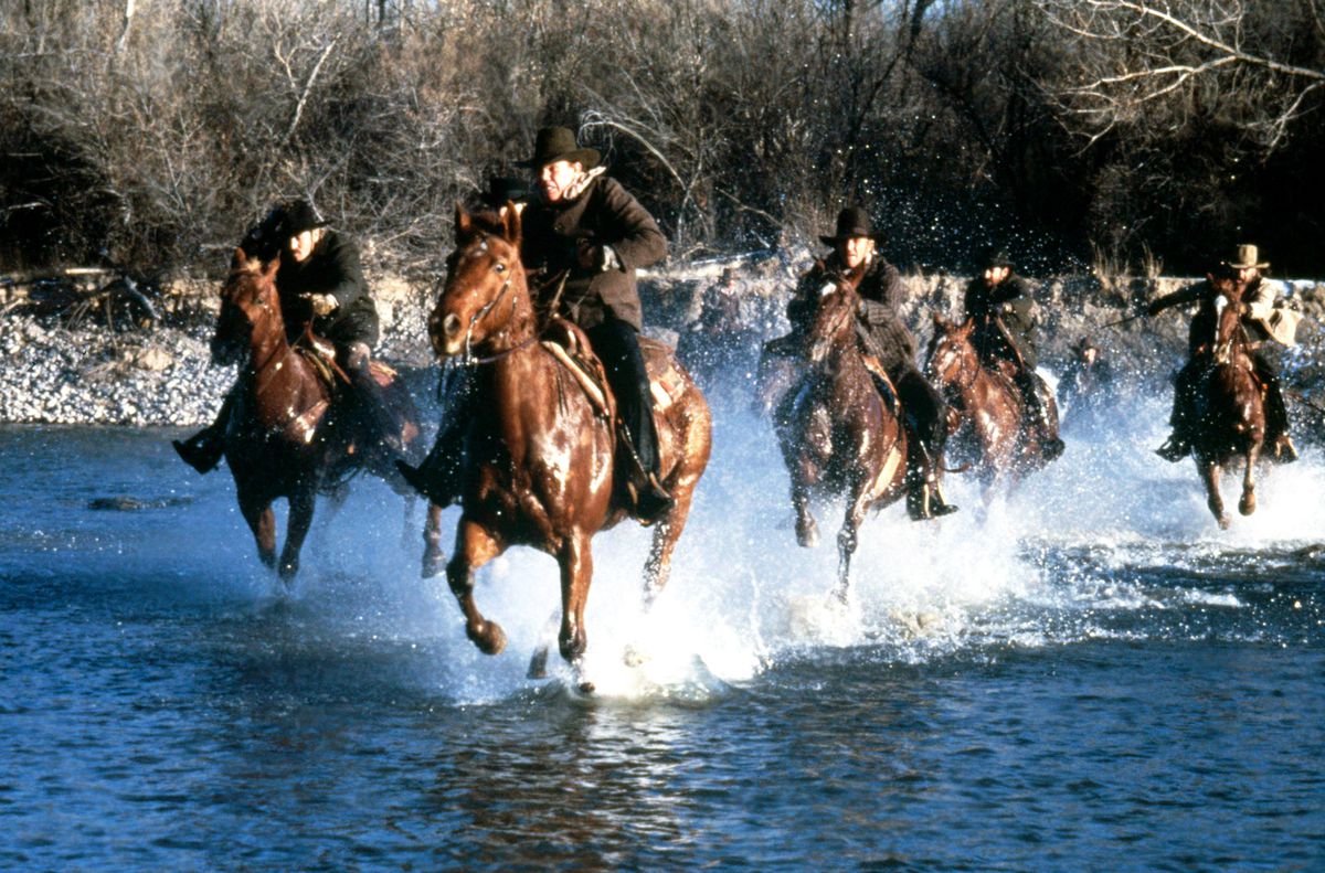 A group of cowboys on horses cross a river in Silverado