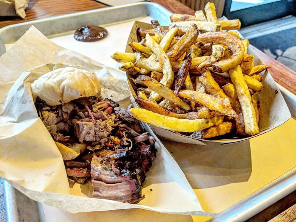 Barbecue-style brisket sandwich and a side of fries on a metal tray