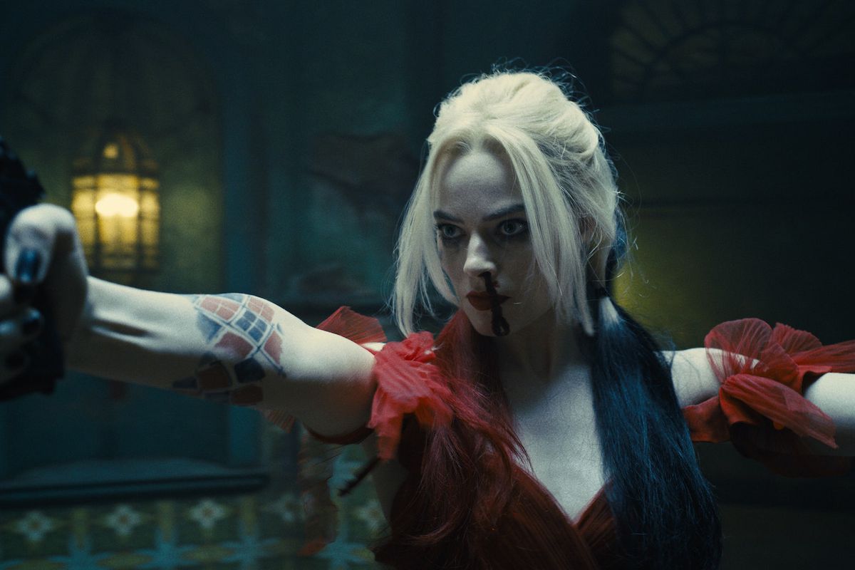 Harley Quinn points a gun at someone, blood dripping down her face. She’s wearing a lovely ballgown.