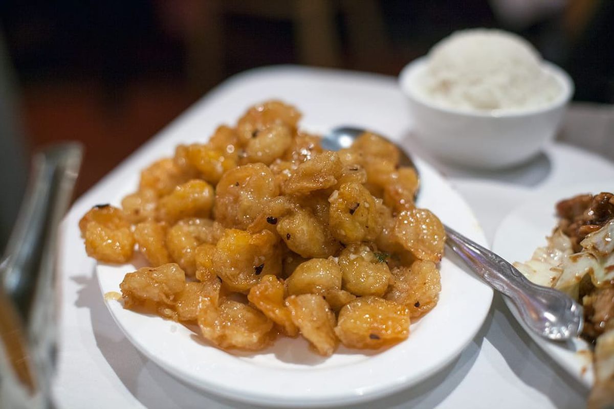 A plate of crispy shrimp on a wide white plate with spoon for serving.