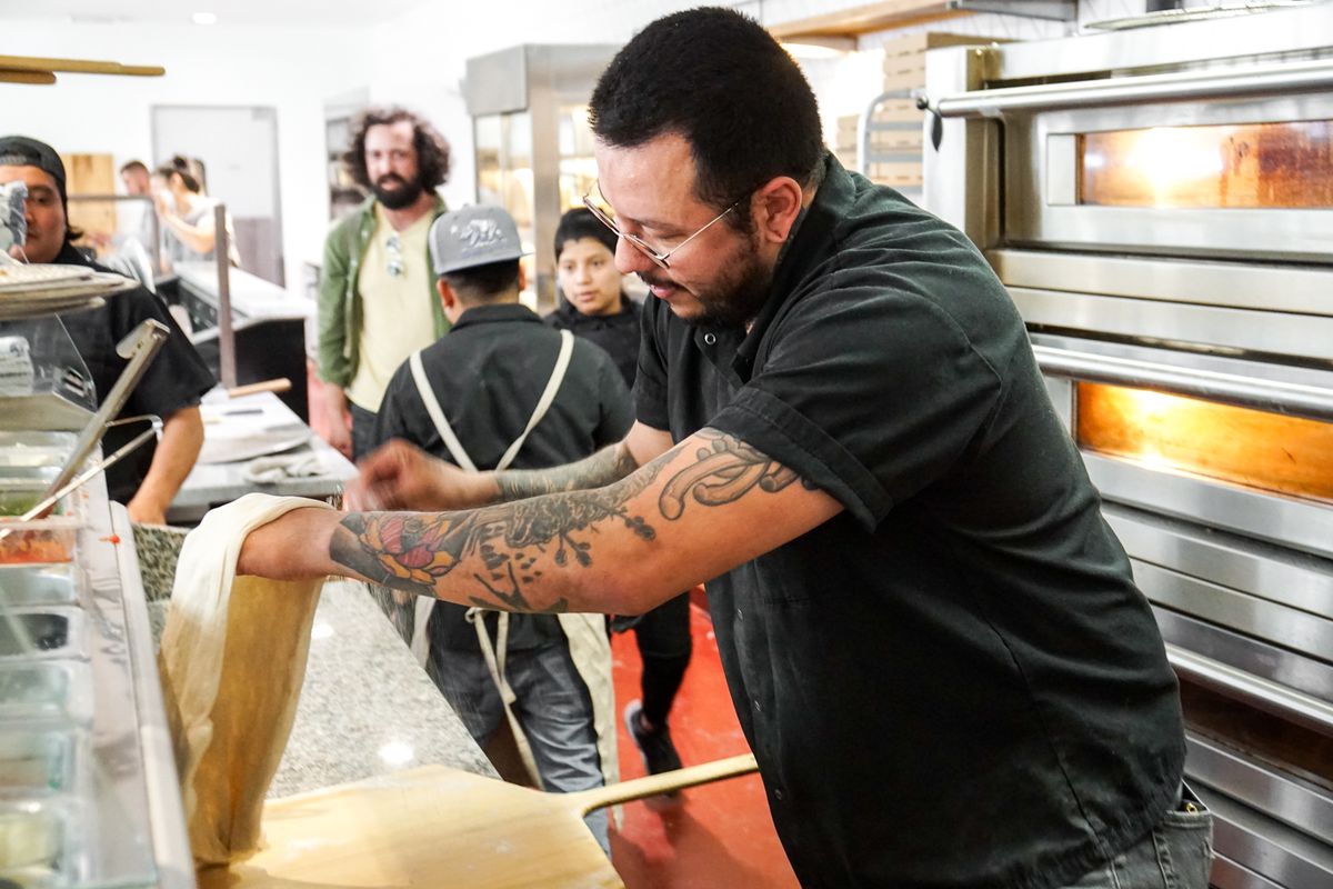 A tattooed pizza chef stretches dough in front of an electric oven at Pane Bianco.