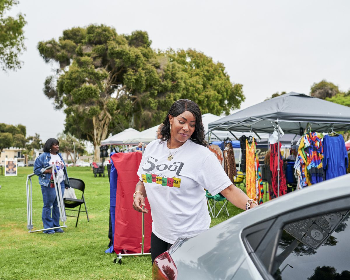 Shala Waines opens the trunk of her car. Behind her on a grassy expanse are tents with merchandise.
