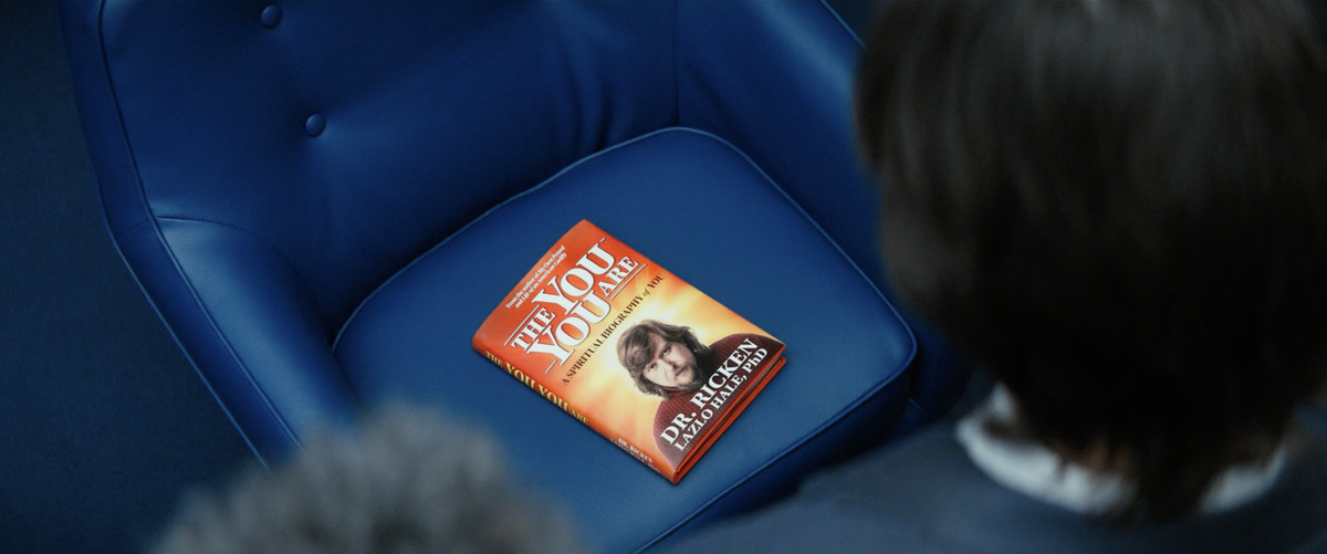 Ricken’s book sitting on a blue chair with the innies of Lumon looking down on it in Severance