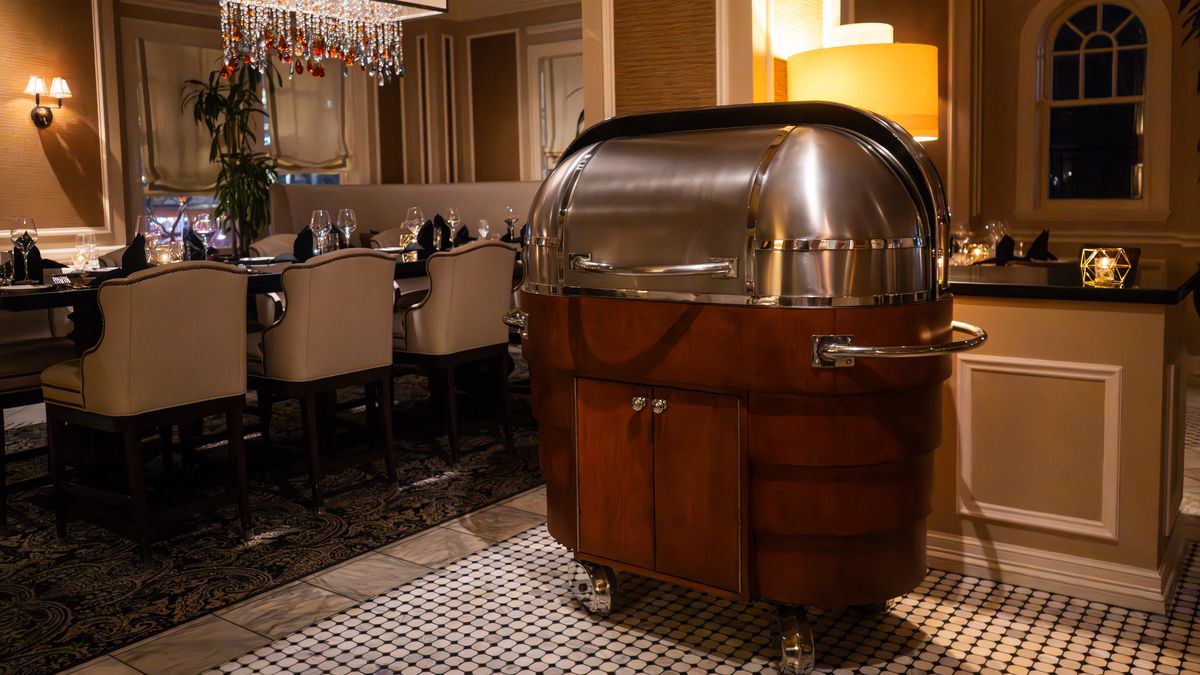 A prime rib cart with a metal top and wooden body sits in the middle of a restaurant.