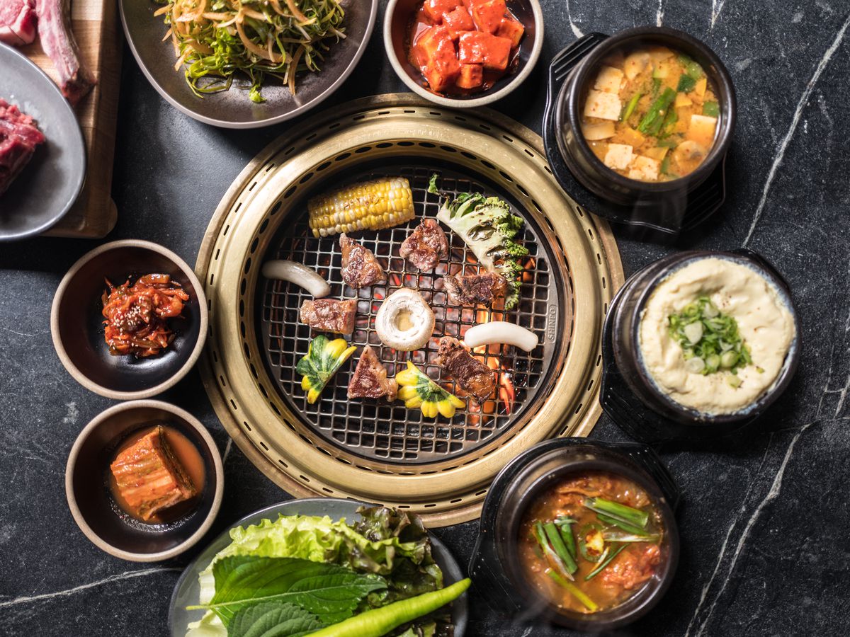 A circular beef-filled tabletop grill sits at the center; around that gold-rimmed grill are small banchan, including kimchi and egg omelet