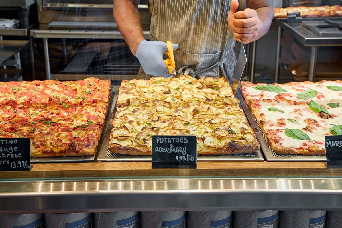 a variety of pizzas being sliced by hand