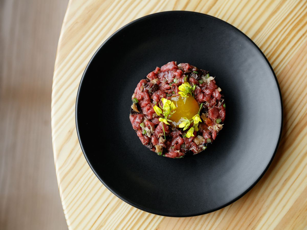 Steak tartare on a black plate with yellow flowers sprinkled atop a small egg yolk at Marrow