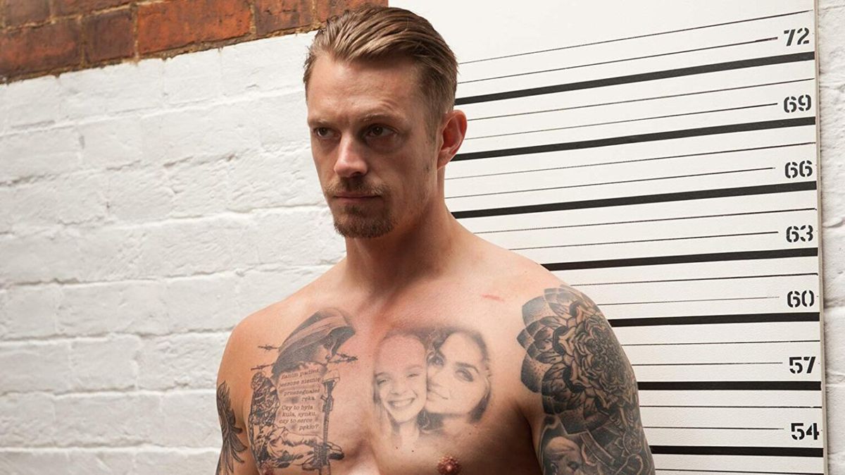 A shirtless, heavily tattooed Joel Kinnaman stands in front of a wall with height measurement in The Informer