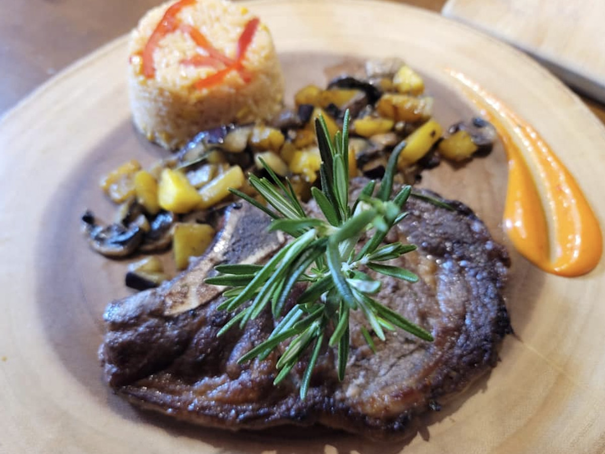 A marinated steak on a plate alongside rice and seasoned vegetables. 
