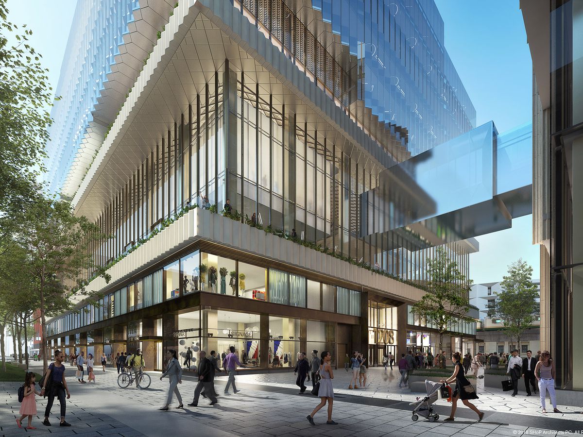 Rendering of the first few floors of a huge glass skyscraper. People walk and bike on the street outside, and there’s many more seen through the windows of the building. 