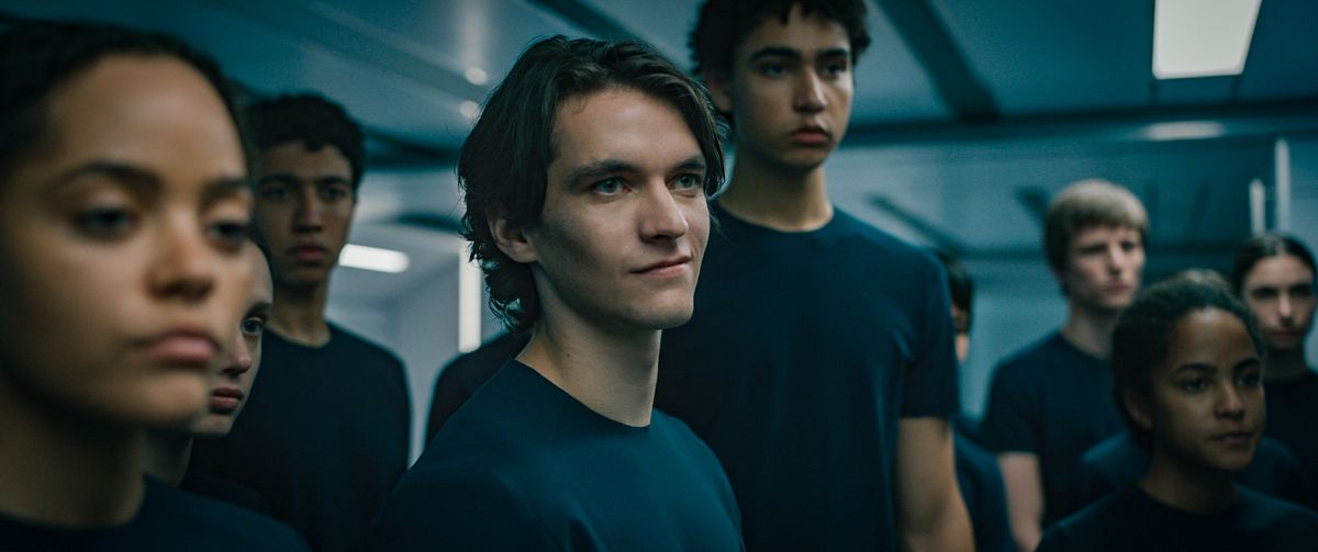 Fionn Whitehead smirks rebelliously amid a crowd of blank-faced teenagers in Voyagers