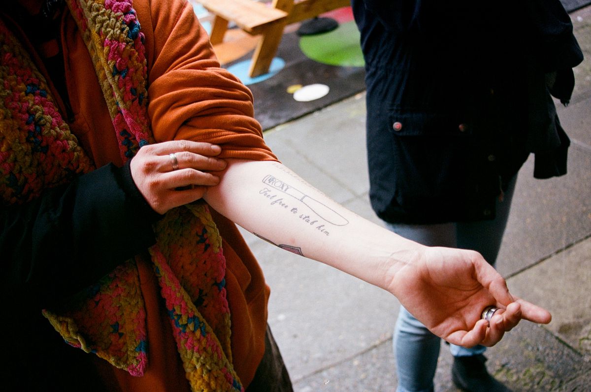 A person exposes their forearm, showing a tattoo of a knife with the Roxy logo on it. “Feel free to stab him” is written in cursive below the knife.