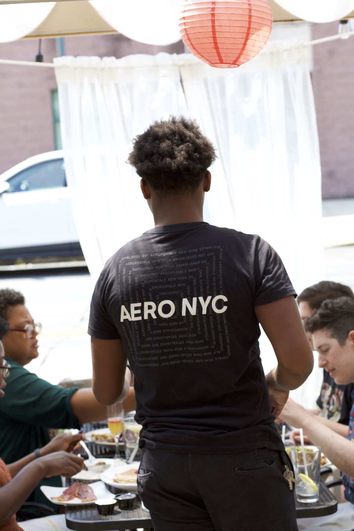 A server at a restaurant wears a shirt that reads Aero NYC on the back, while a table of four women eats brunch.