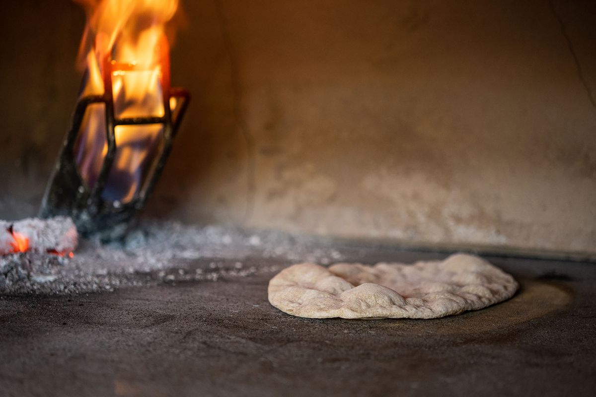 A tan pita bubbles up inside of a wood-fired oven.