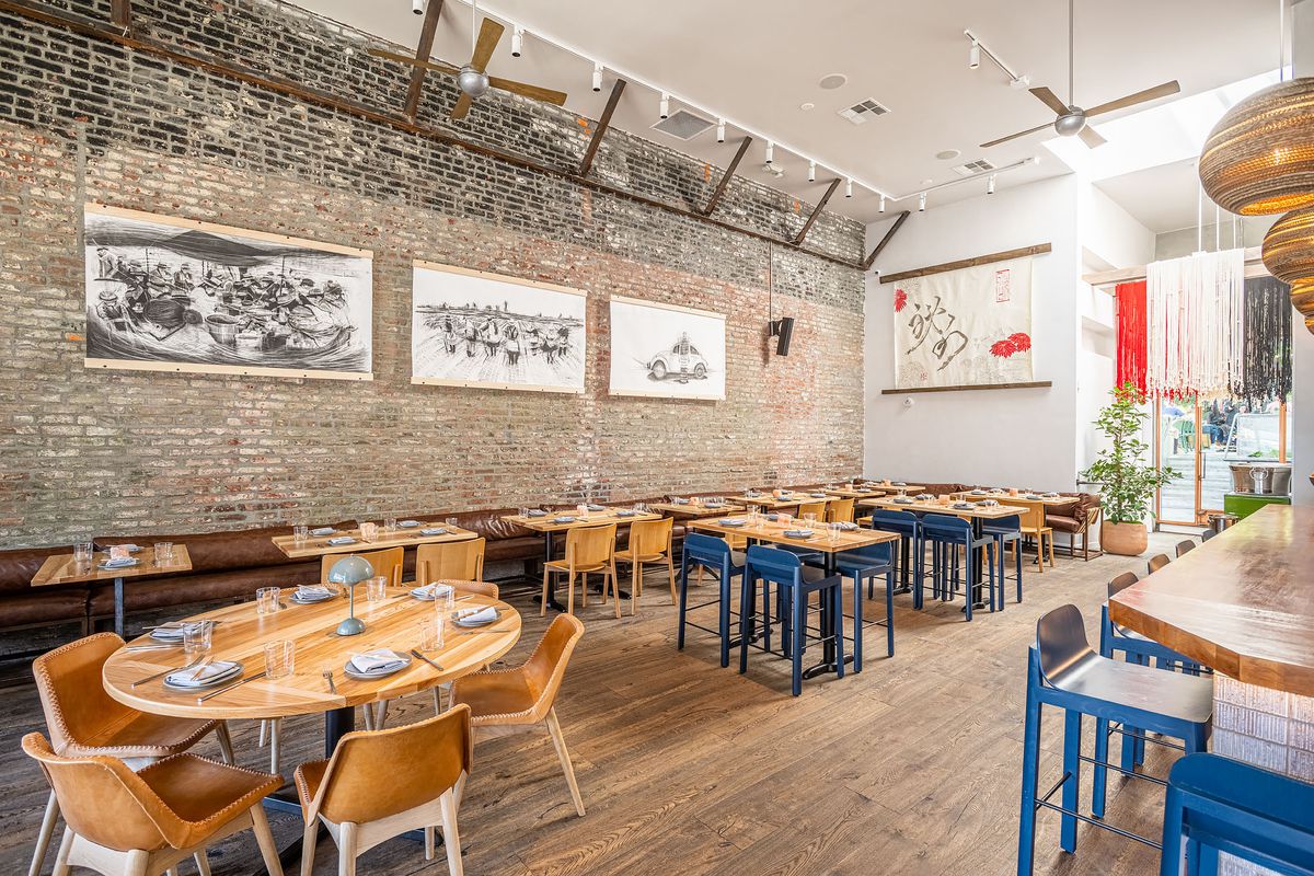 Dining area with wood tables, brick wall, paintings, and wood floors.