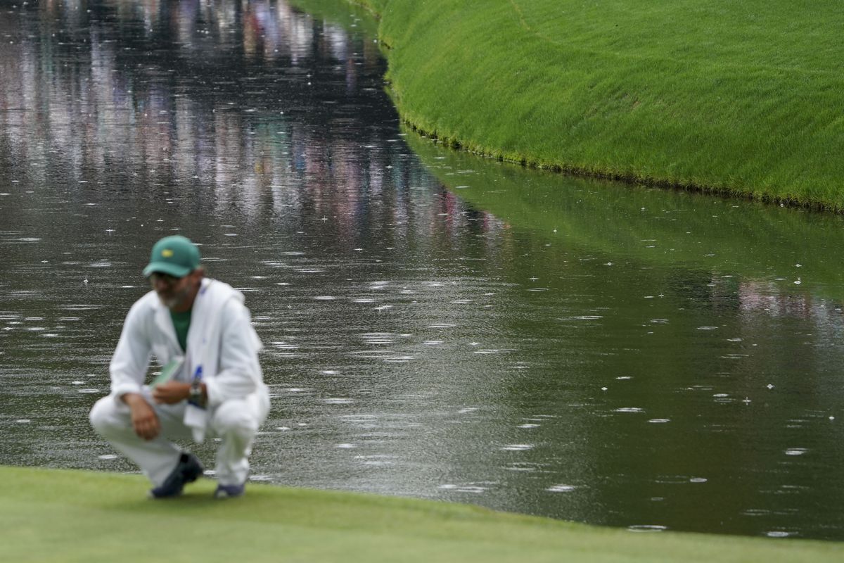 Corey Conners caddie surveys the no. 16 green as rain hits the pond behind him during the second round of The Masters golf tournament.
