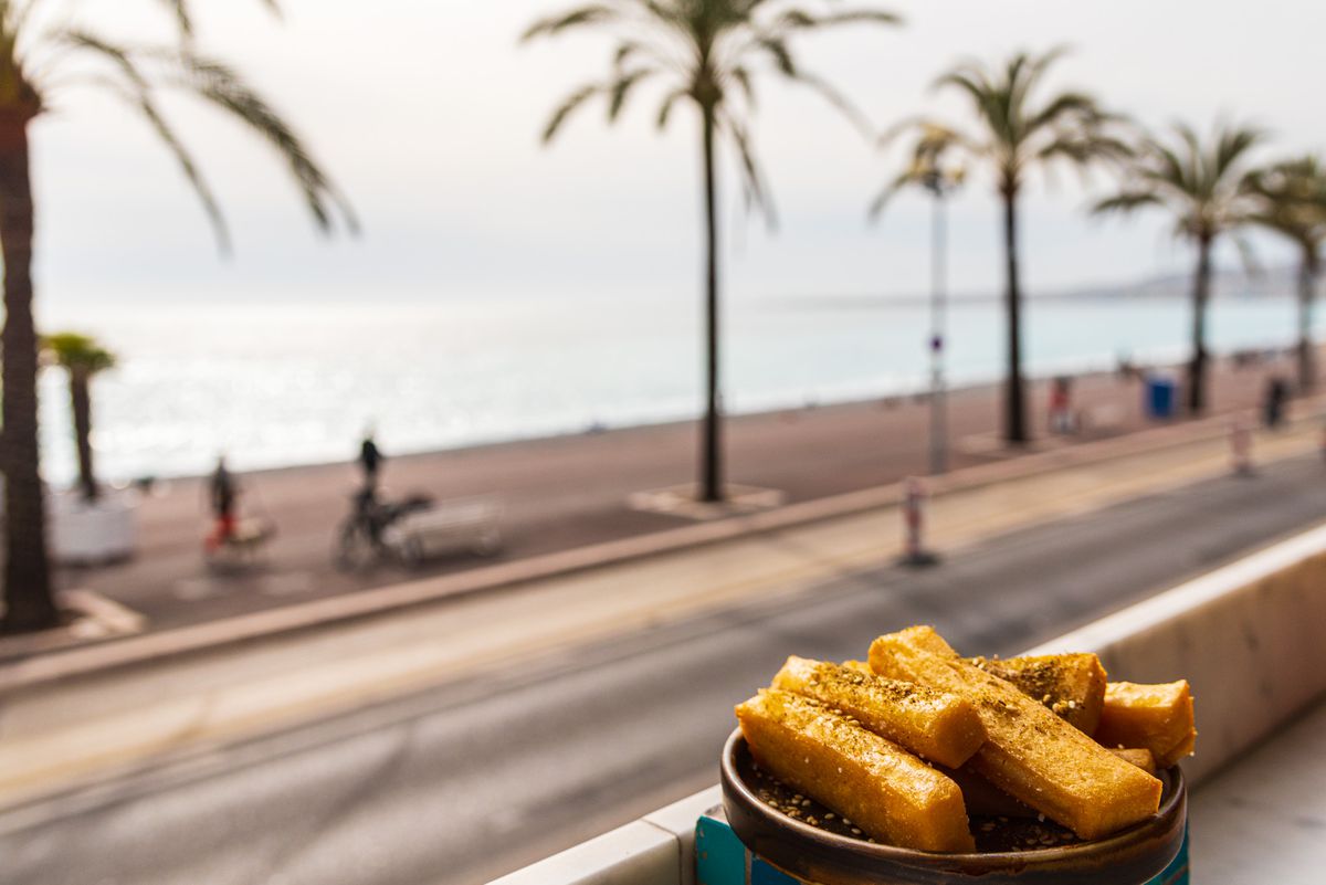A bowl of panisse set in front of a view of the street, palm trees, and the sea beyond.