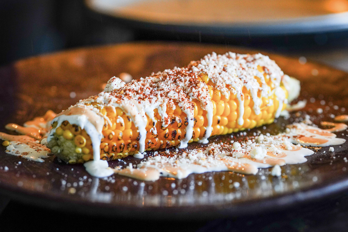A long shot of corn on the cob with sour cream on a dark plate.