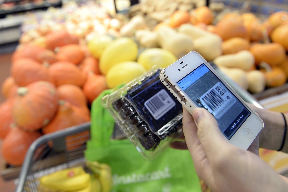 A hand holding a phone with the Instacart app on it, in front of a box of fruit