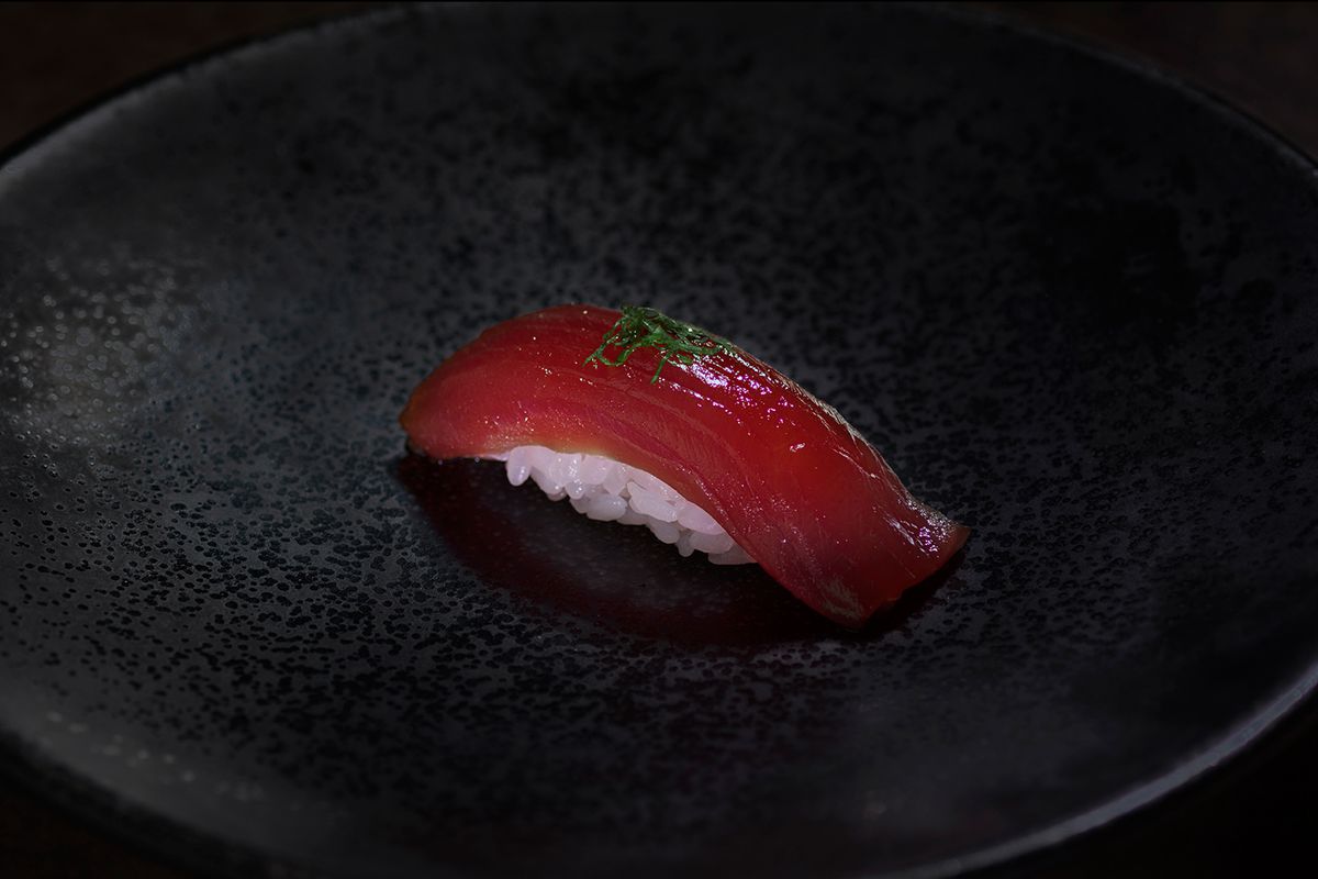 A piece of tuna nigiri on a round black plate.