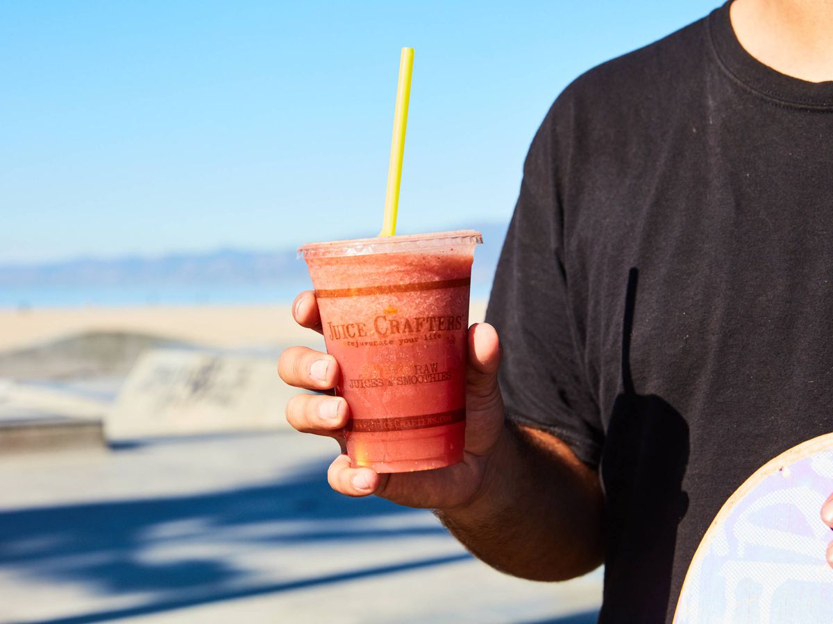 A man on the beach holds a smoothie.