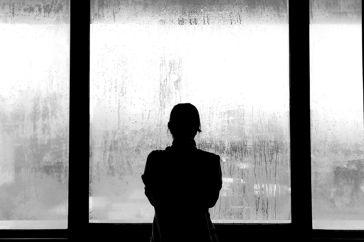 A young woman standing with her back to the camera, looking through frosted glass.