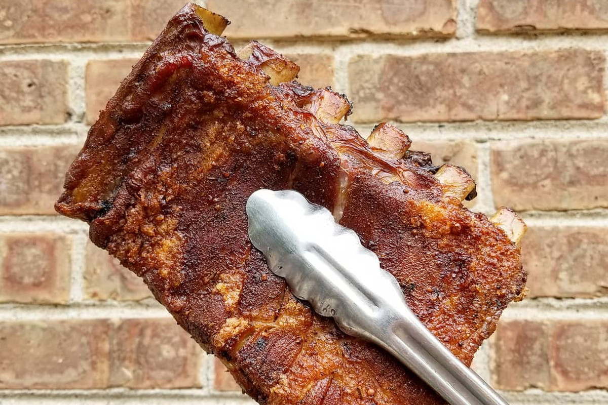 A half slab of barbecue baby back ribs held with metal tongs.