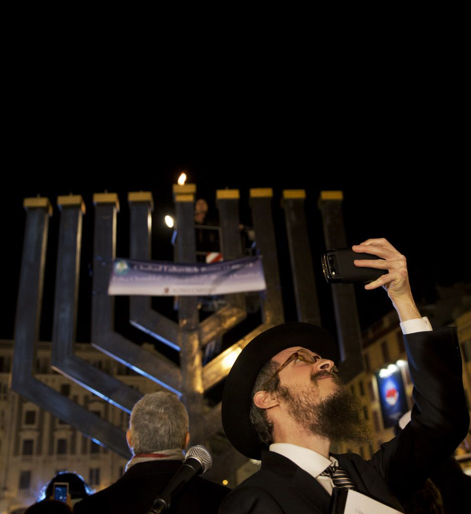 The Rev. Shalom Hazan, foreground, takes a selfie as Mr. Mossi Fadlun lights the candles on the top of a giant menorah celebrating Hanukkah, the Jewish festival of lights, in Rome on Sunday. | AP Photo/Alessandra Tarantino