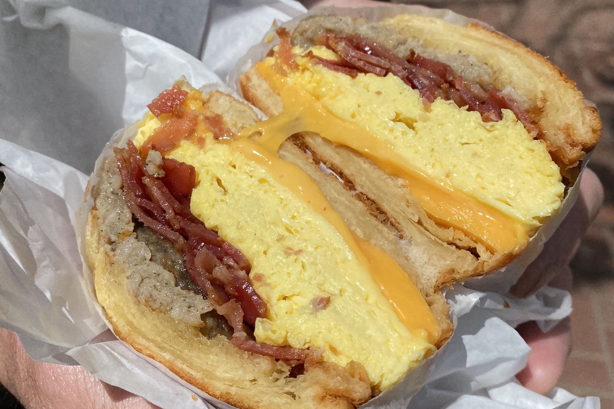 A breakfast sandwich cut in half with bacon and sausage.
