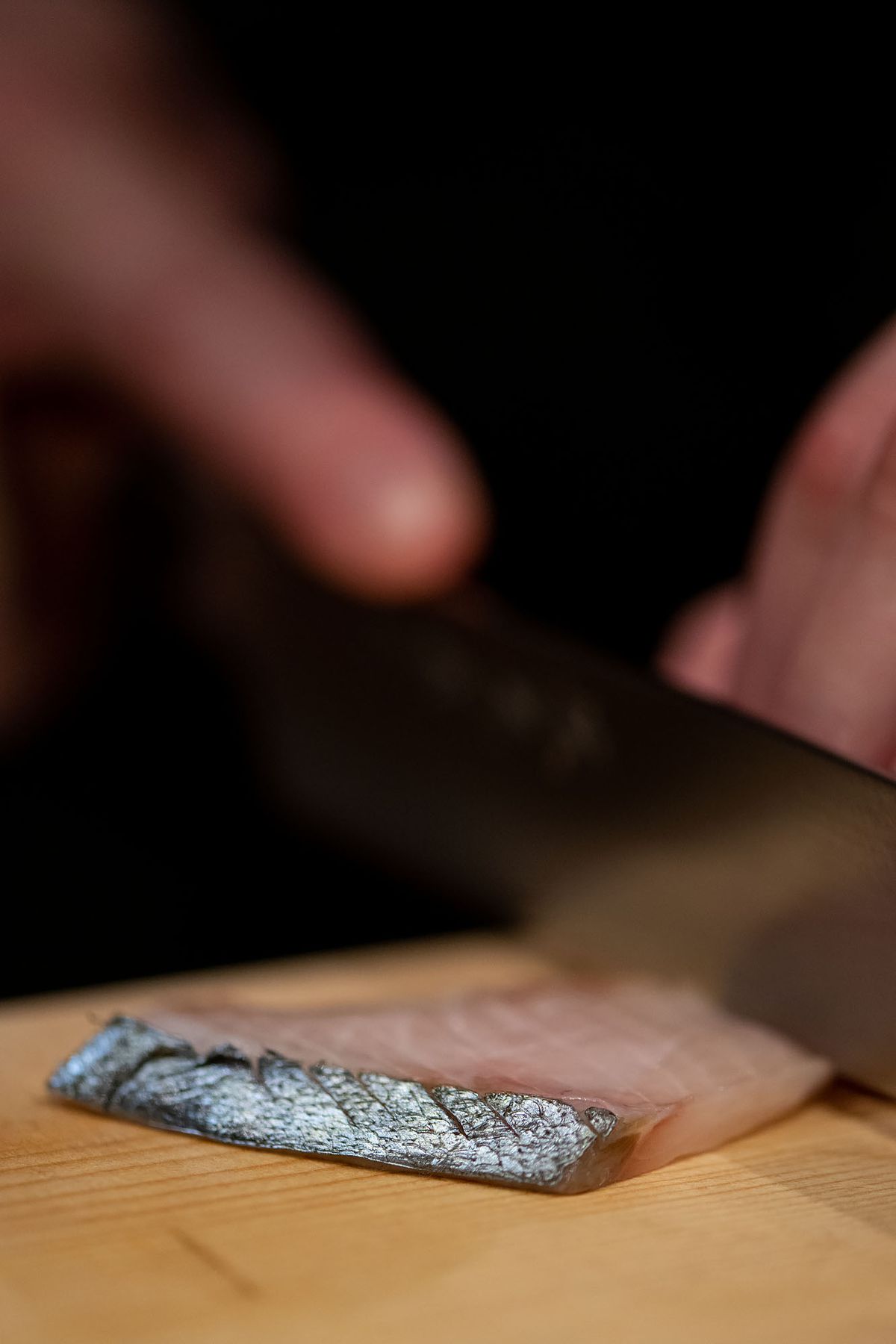Close up of slicing fish with knife on cutting board.