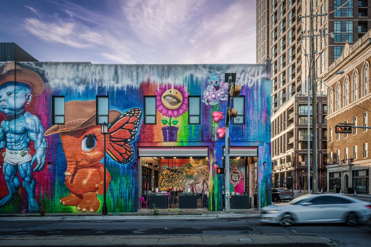 A mural shows a muscled, blue baby alien, an orange elephant in a cowboy hat with butterflies for ears, a pink sunflower with a human face, and an alien in a ship.