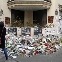 A woman looks at flowers laid near the headquarters of magazine Charlie Hebdo in Paris, Friday Feb. 6, 2015. Brothers Said and Cherif Kouachi killed 12 people in a terror attack at the offices of French satirical publication Charlie Hebdo on Jan. 7. The two gunmen, were killed by French police two days later. 