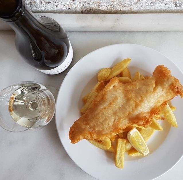 Fried fish on a pile of fries, with a glass of white wine nearby and a bottle