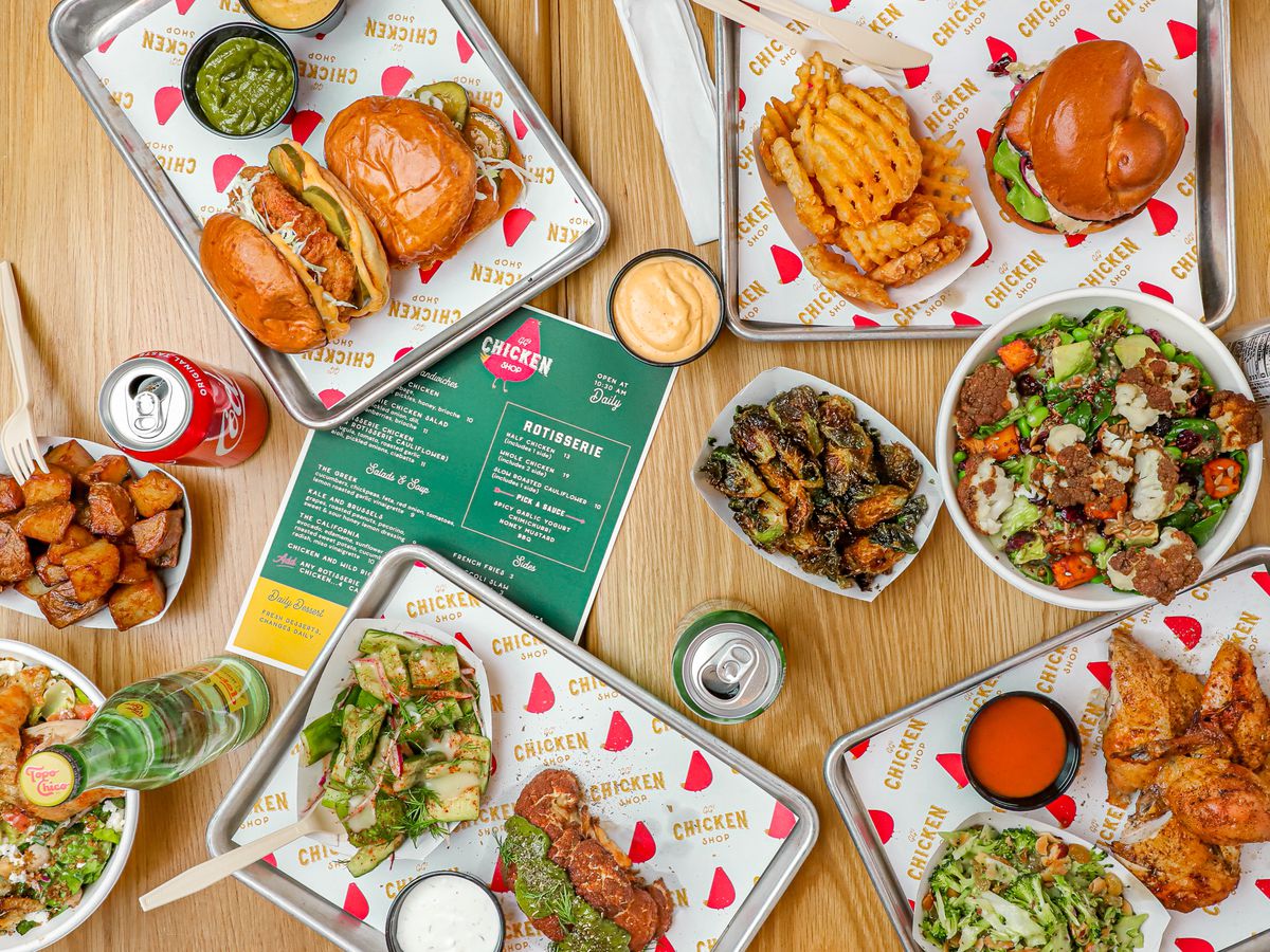 A wooden table covered with metal trays with food from waffle fries, salads, to chicken.