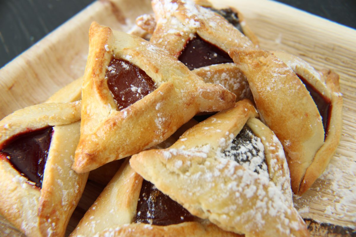 A pile of triangle-shaped hamantaschen cookies on a plate dusted with powdered sugar.