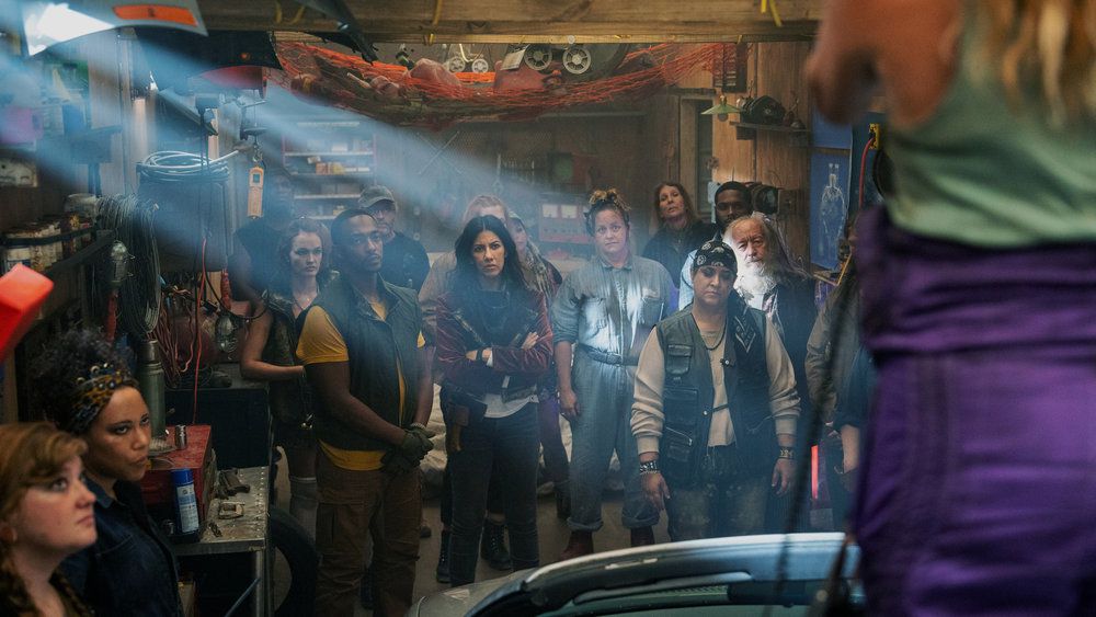 Anthony Mackie’s John Doe and Stephanie Beatriz’s Quiet are assembled with a group of wasteland raiders in front of a speaker just off-screen in the Peacock series Twisted Metal