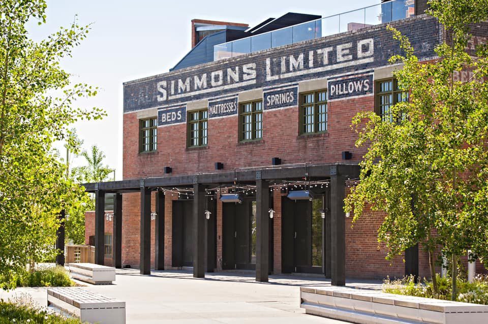 A red brick factory exterior, printed with the name Simmons Limited, with a patio awning out front strung with lights