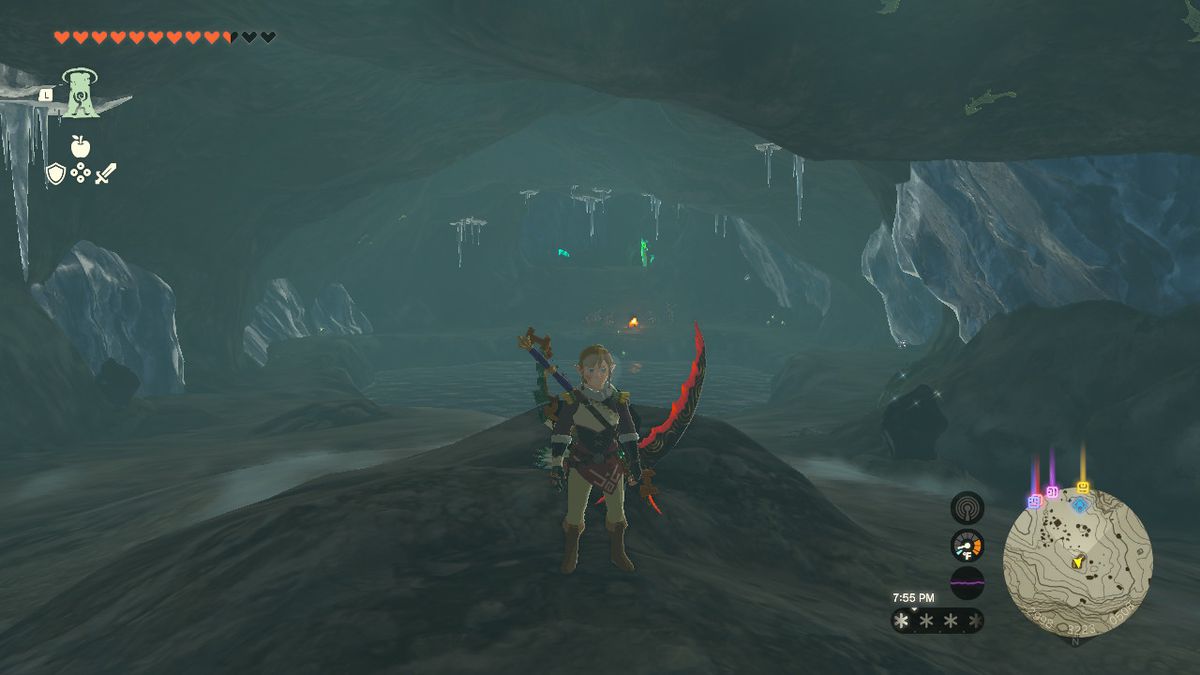 Link stands on a small rock mound facing the inside of a cave with a pond at the center