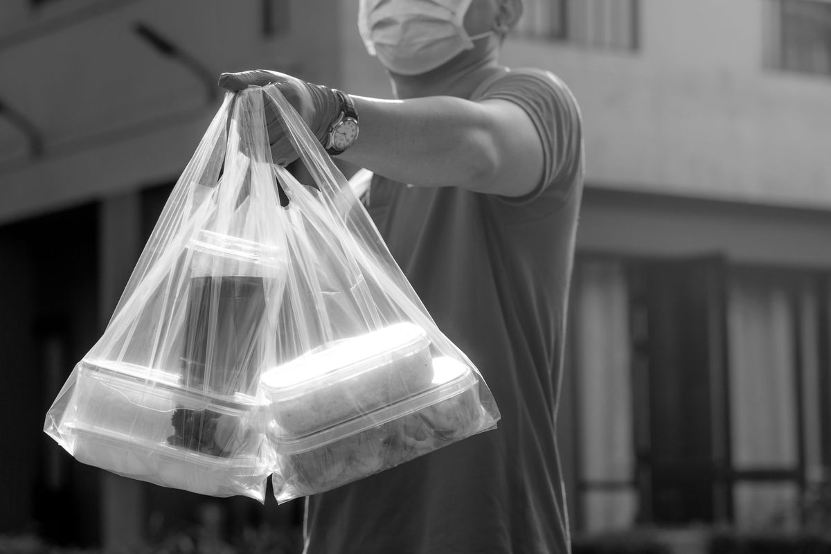 A black and white image of a clear bag containing four full takeout containers and a drink.