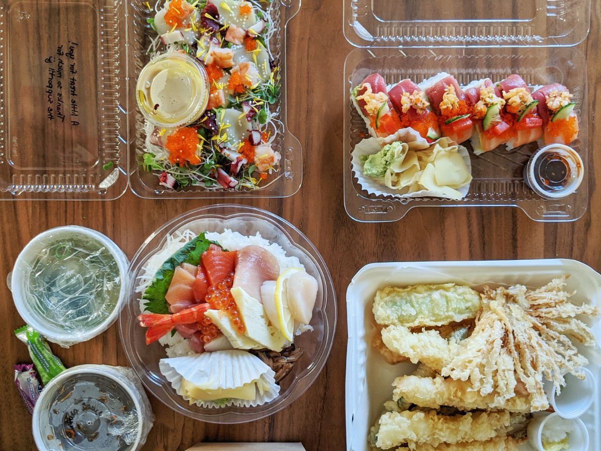 From above, takeout containers filled with various dishes on a wooden table