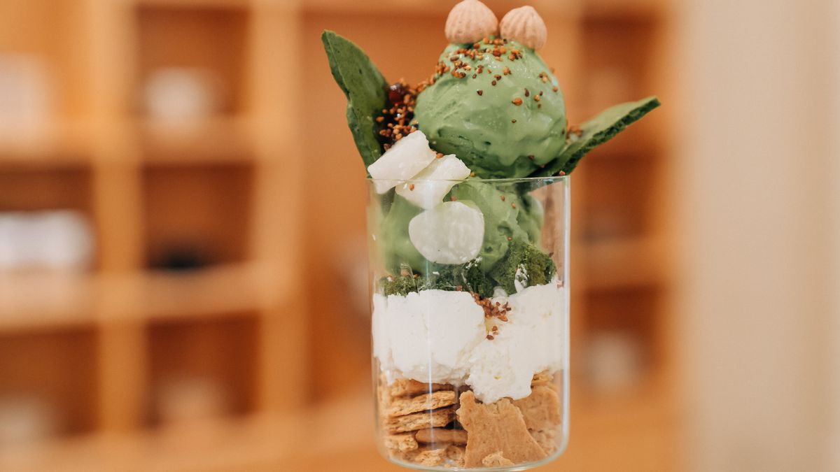 A clear, stemmed glass filled with crushed graham crackers, dollops of whipped cream, and green matcha gelato.