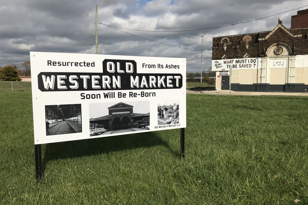 A sign in a grassy lot with photos of an old brick, open-air market  that says “Old Western Market.”