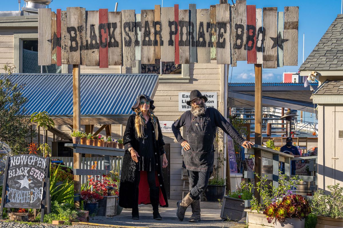 Chef Tony Carracci and partner Miss Suzie stand beneath the sign for Black Star Pirate BBQ in Richmond, California.