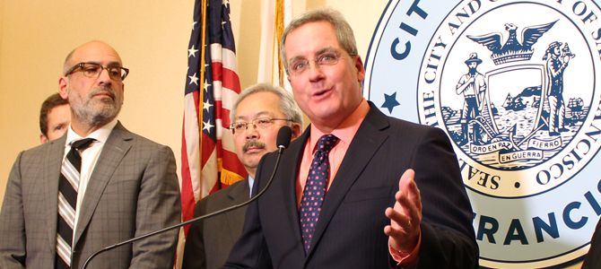 City Attorney Dennis Herrera standing at a podium in front of the city seal, with the late mayor Ed Lee at his right.